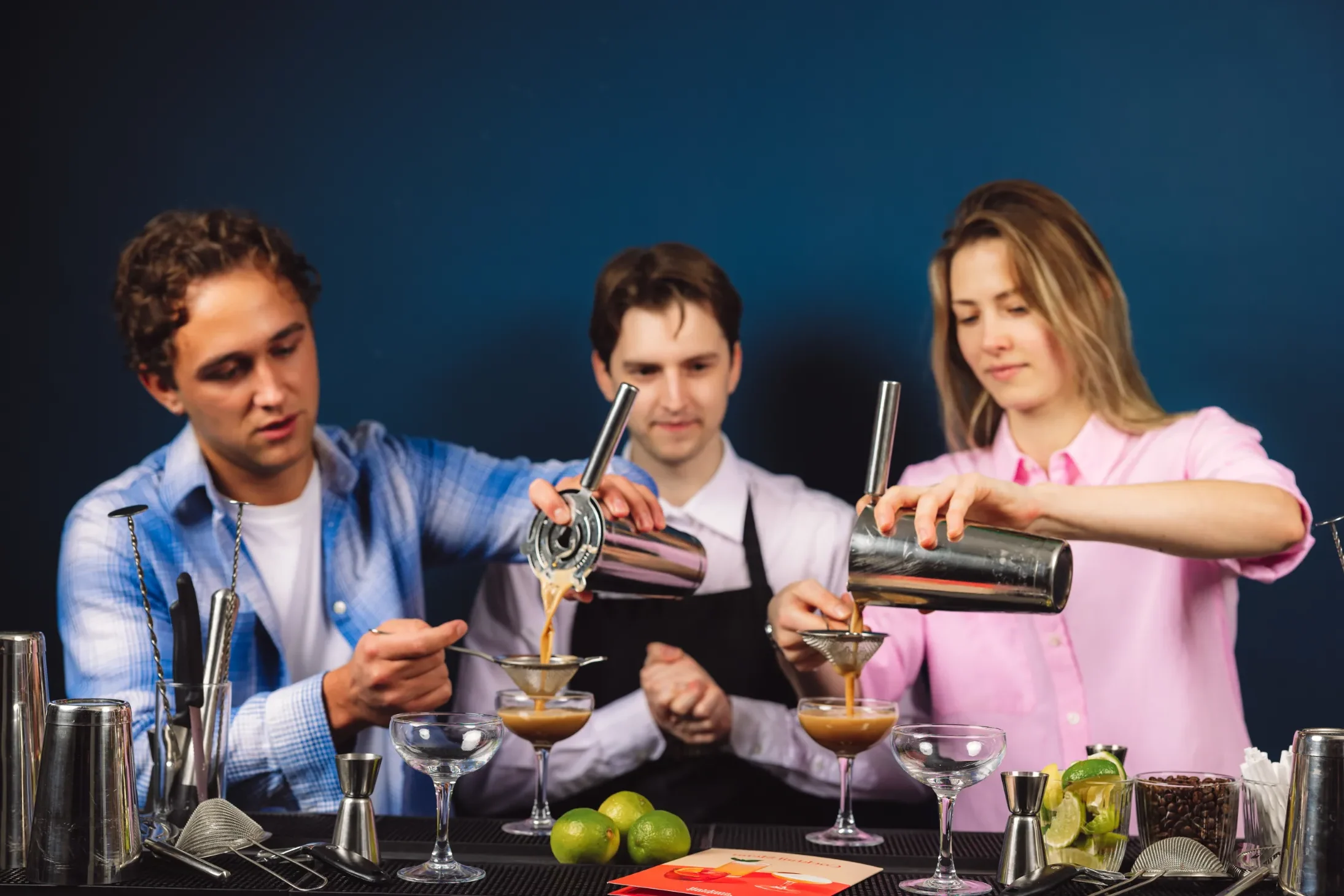 Tre personer deltager i et cocktailkursus og lærer at mixe cocktails med professionelle bartendere